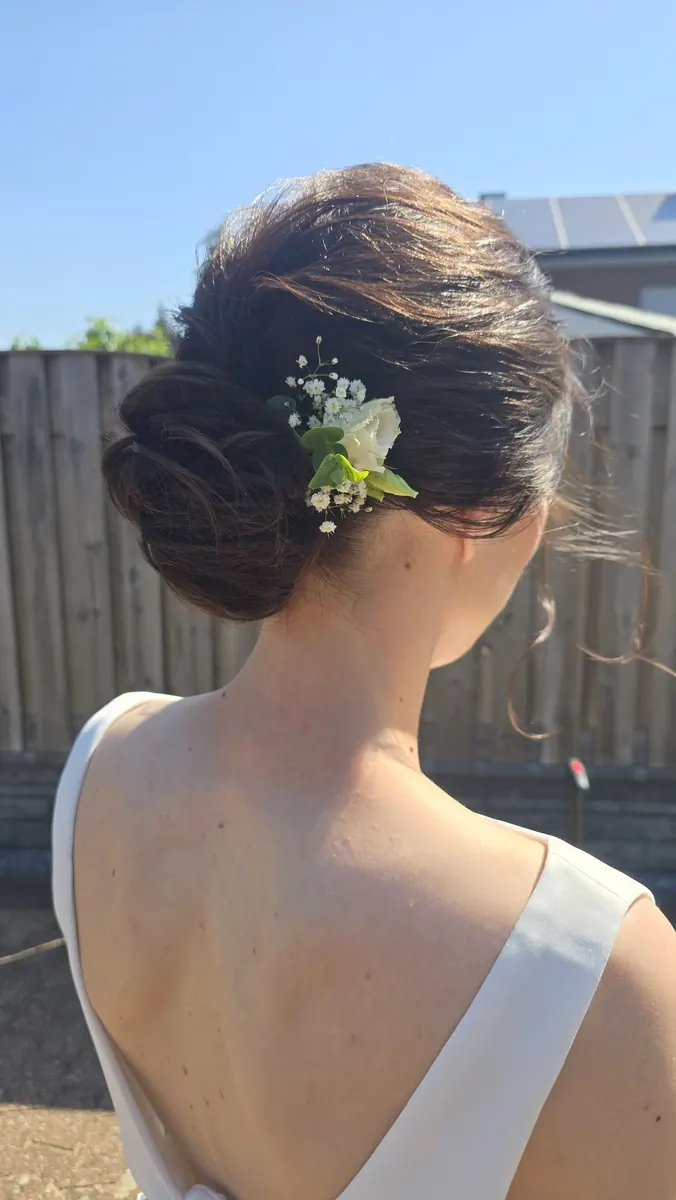 Eleganter tiefer Brautdutt mit frischer Blüte